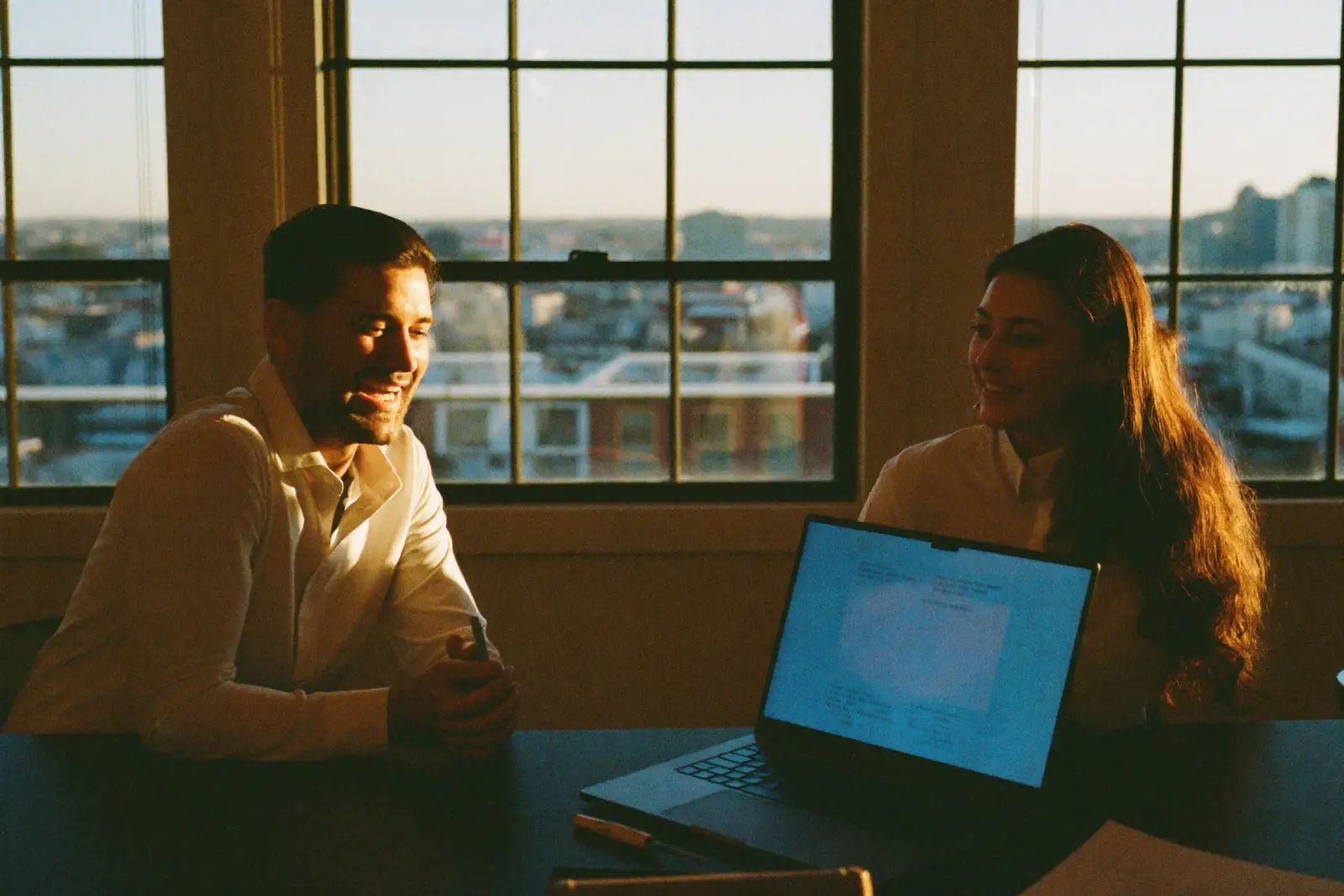 An agency account manager and a small business owner review results together at golden hour, both smiling, a laptop open between them