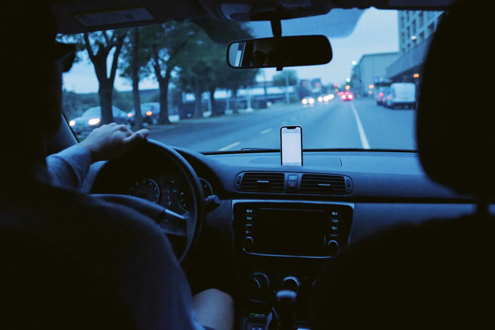A real estate agent drives at dusk with a phone mounted on the dashboard