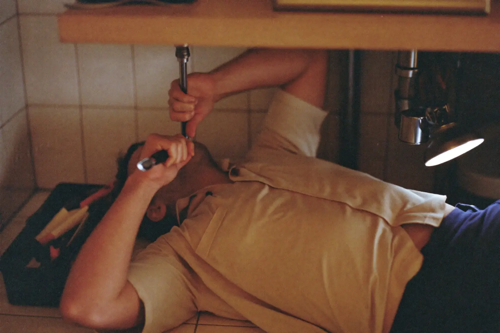 A plumber works under a kitchen sink with a wrench