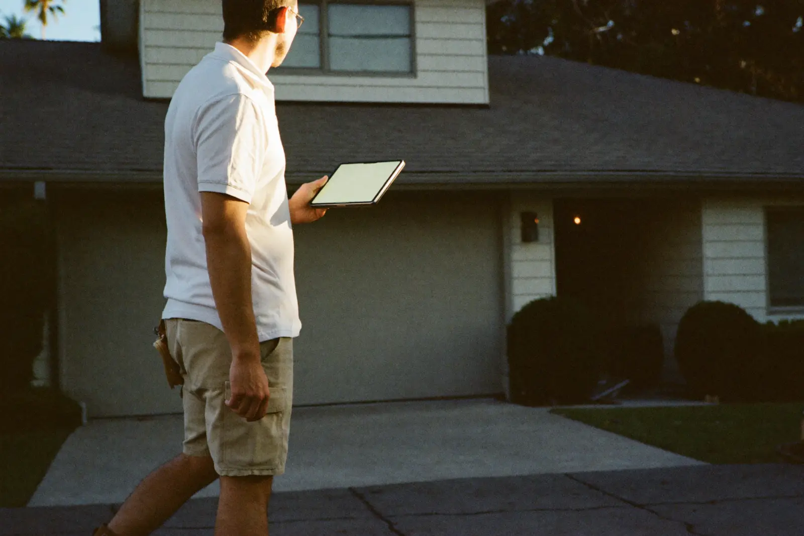 A roofing estimator with a tablet studies a house roof in late afternoon light