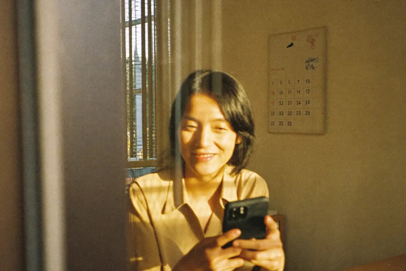 A small business owner at her desk in late-afternoon light, smiling as she reads a booking notification on her phone