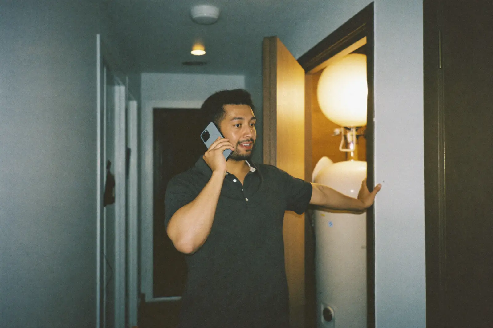 A homeowner on the phone in a dim hallway at night, standing beside an open utility closet