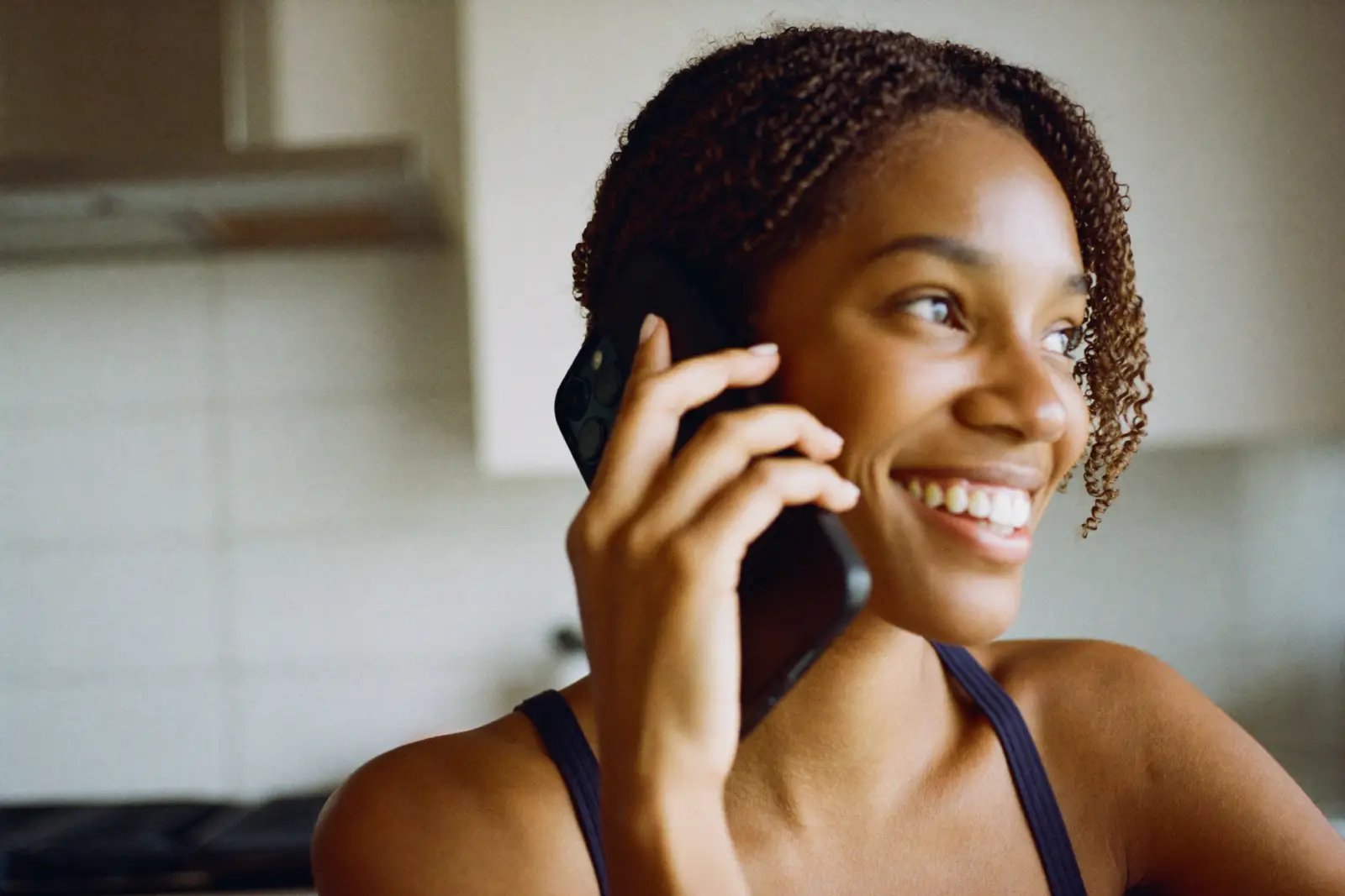 A smiling woman answers a phone call in her kitchen in the early evening